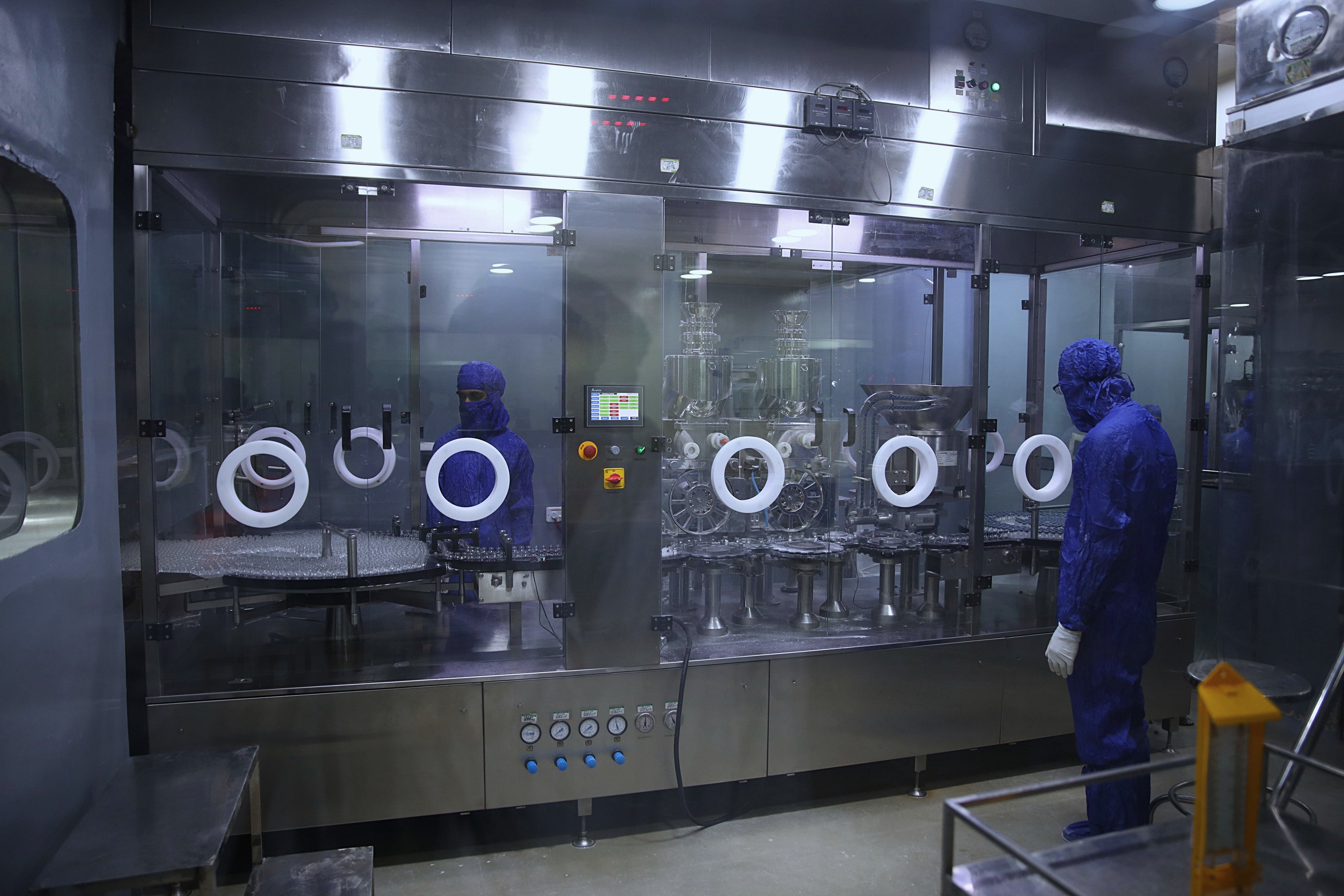 Opérateurs en tenue de salle blanche devant une ligne de remplissage aseptique en acier inoxydable, sous isolateur vitré